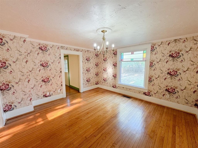 empty room with hardwood / wood-style flooring, ornamental molding, a textured ceiling, and an inviting chandelier