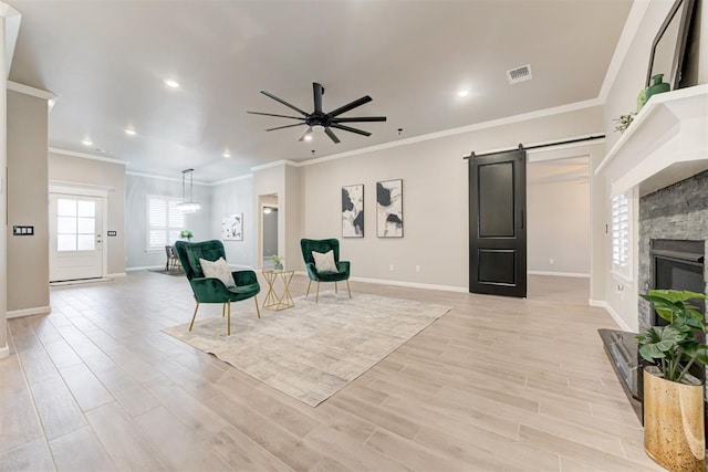 interior space with a stone fireplace, crown molding, light hardwood / wood-style flooring, ceiling fan, and a barn door