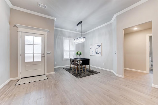 foyer entrance featuring light wood-type flooring, ornamental molding, and an inviting chandelier