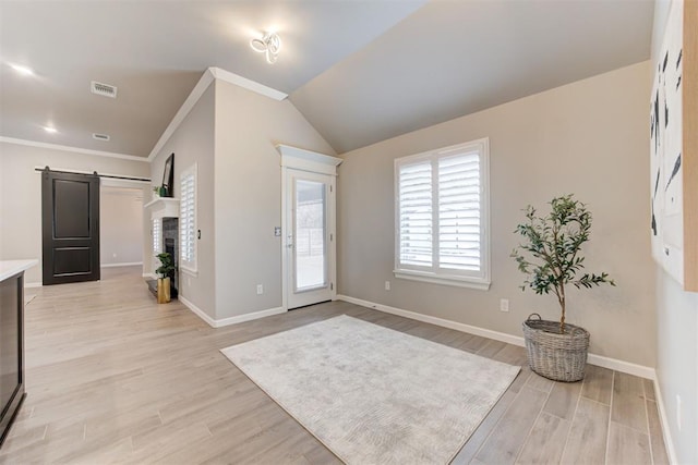 foyer with a barn door, vaulted ceiling, crown molding, and light hardwood / wood-style flooring