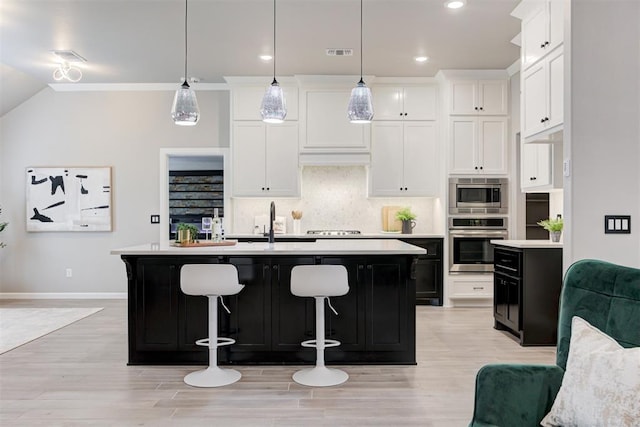 kitchen with an island with sink, light hardwood / wood-style floors, decorative light fixtures, white cabinets, and appliances with stainless steel finishes