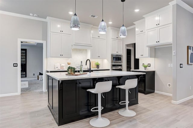 kitchen featuring appliances with stainless steel finishes, tasteful backsplash, a center island with sink, white cabinetry, and hanging light fixtures