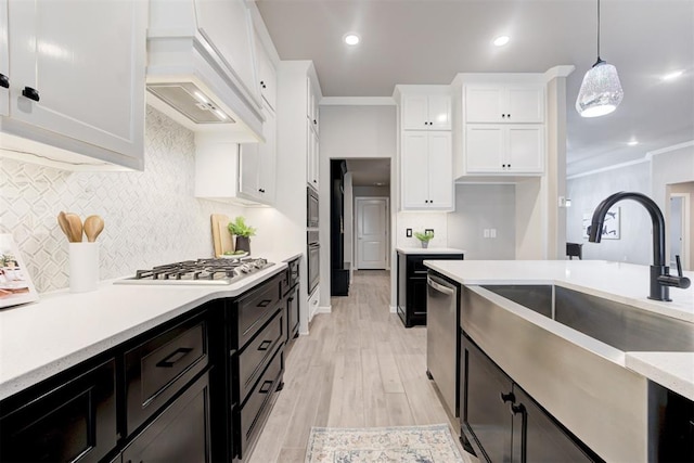 kitchen with light wood-type flooring, ornamental molding, sink, pendant lighting, and white cabinetry