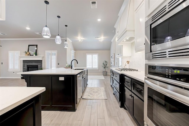 kitchen with white cabinetry, sink, stainless steel appliances, a stone fireplace, and a center island with sink