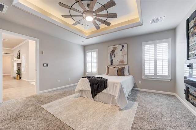 bedroom featuring a tray ceiling, ceiling fan, crown molding, and light colored carpet