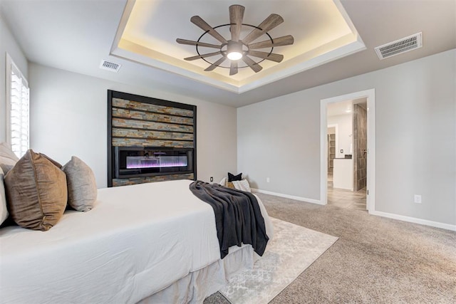 bedroom with a raised ceiling, a stone fireplace, ceiling fan, and carpet