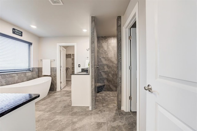 bathroom featuring shower with separate bathtub, vanity, and tile walls