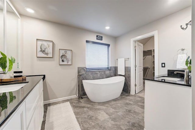 bathroom featuring a washtub, tile walls, and vanity