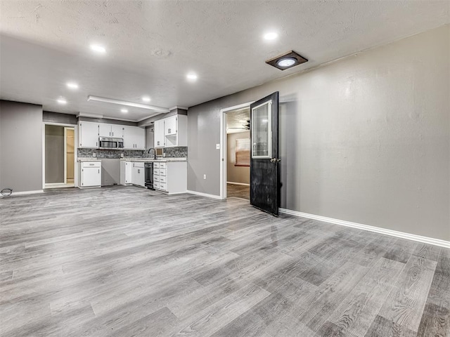 unfurnished living room with sink, a textured ceiling, and light wood-type flooring