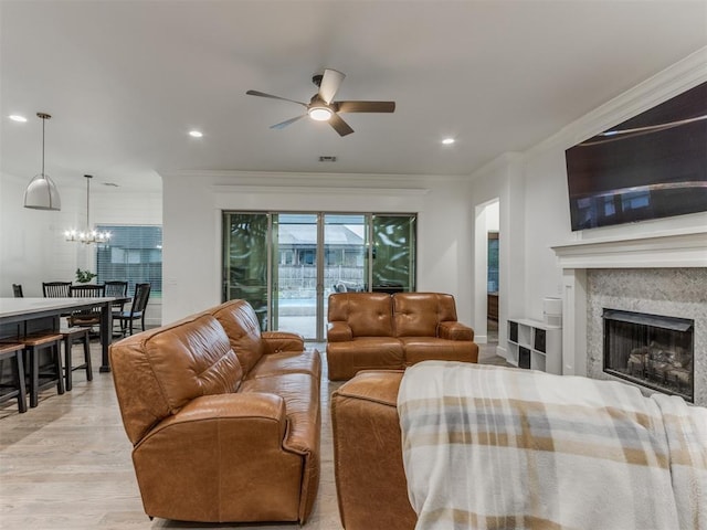 living room with ceiling fan with notable chandelier, a high end fireplace, ornamental molding, and light wood-type flooring