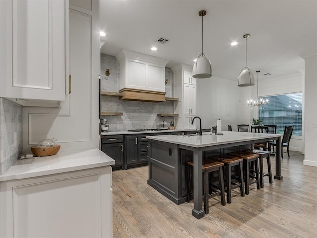 kitchen with white cabinetry, hanging light fixtures, light wood-type flooring, a kitchen breakfast bar, and an island with sink