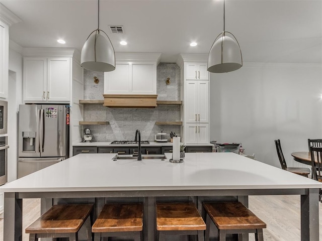 kitchen featuring hanging light fixtures, tasteful backsplash, a center island with sink, and white cabinets