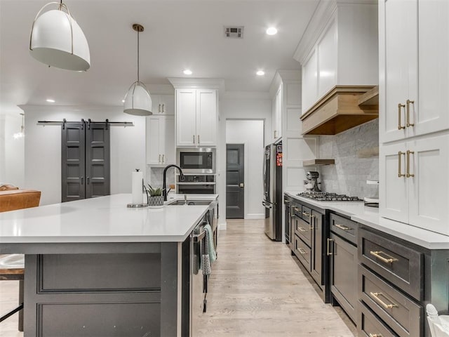 kitchen with appliances with stainless steel finishes, a barn door, decorative light fixtures, and white cabinets