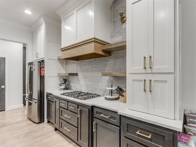 kitchen featuring appliances with stainless steel finishes, white cabinetry, decorative backsplash, crown molding, and light wood-type flooring