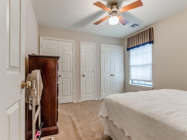 bedroom with two closets, light colored carpet, and ceiling fan