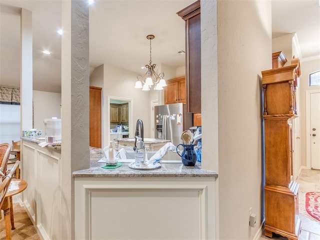 kitchen with sink, light stone counters, stainless steel fridge, a chandelier, and decorative light fixtures