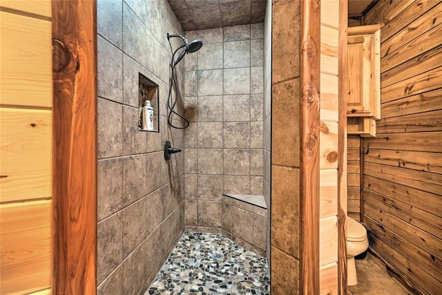 bathroom featuring toilet, a tile shower, and wooden walls