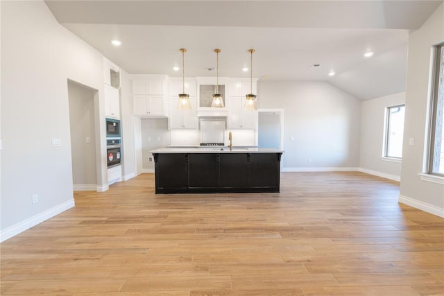 kitchen with stainless steel oven, black microwave, light hardwood / wood-style flooring, an island with sink, and pendant lighting