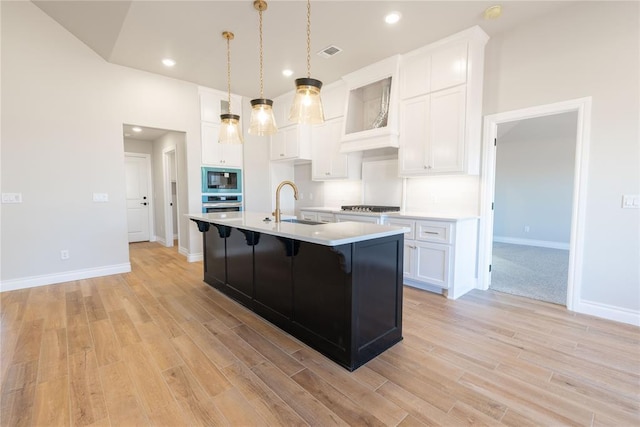 kitchen featuring built in microwave, sink, stainless steel oven, a kitchen island with sink, and white cabinets