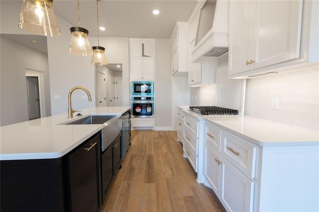 kitchen with custom exhaust hood, hanging light fixtures, an island with sink, stainless steel gas stovetop, and white cabinets