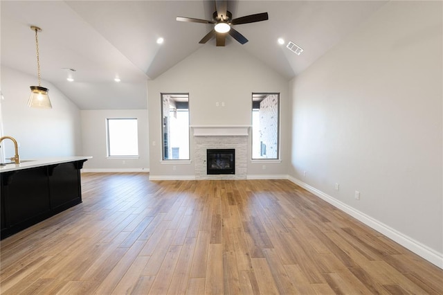 unfurnished living room featuring lofted ceiling, sink, light hardwood / wood-style flooring, ceiling fan, and a stone fireplace