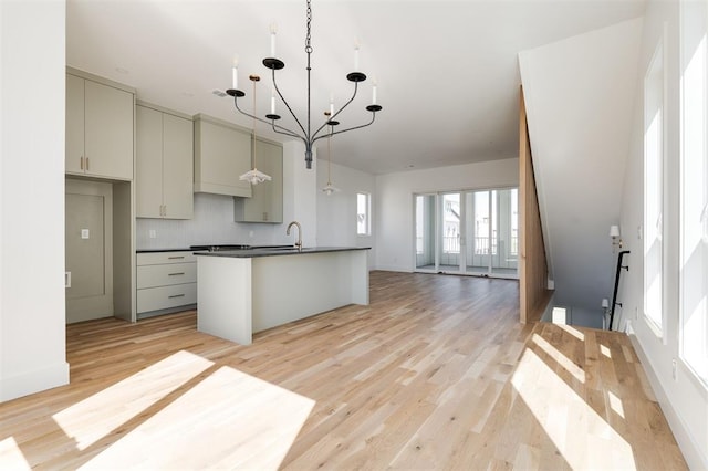 kitchen featuring a kitchen island with sink, a chandelier, dark countertops, light wood finished floors, and open floor plan