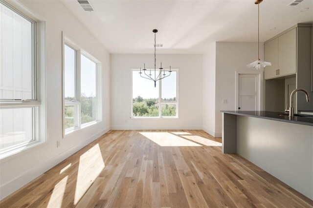 unfurnished dining area with an inviting chandelier, a sink, light wood finished floors, baseboards, and visible vents