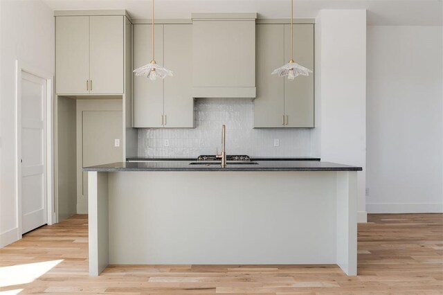 kitchen with dark countertops, decorative backsplash, a sink, and light wood-style floors