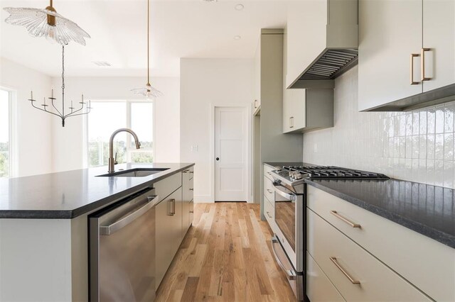 kitchen with dark countertops, wall chimney range hood, light wood-type flooring, a sink, and stainless steel appliances
