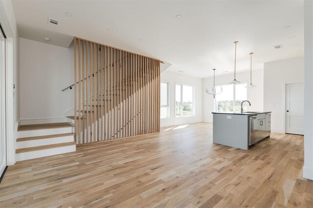 kitchen with a center island with sink, light wood-type flooring, a sink, a chandelier, and open floor plan