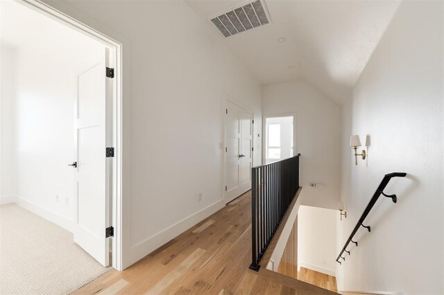 hall with visible vents, vaulted ceiling, baseboards, light wood finished floors, and an upstairs landing