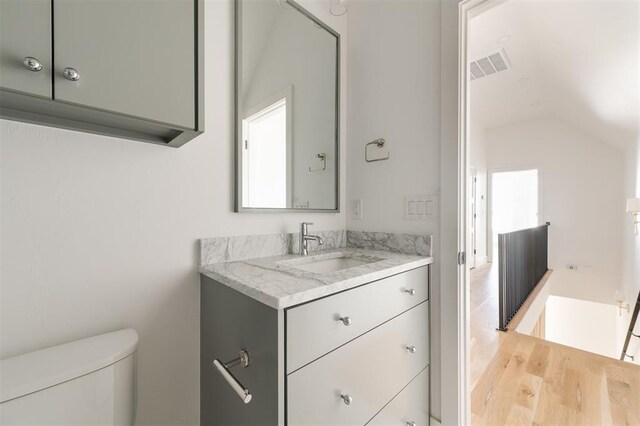 half bathroom with visible vents, vaulted ceiling, wood finished floors, vanity, and toilet