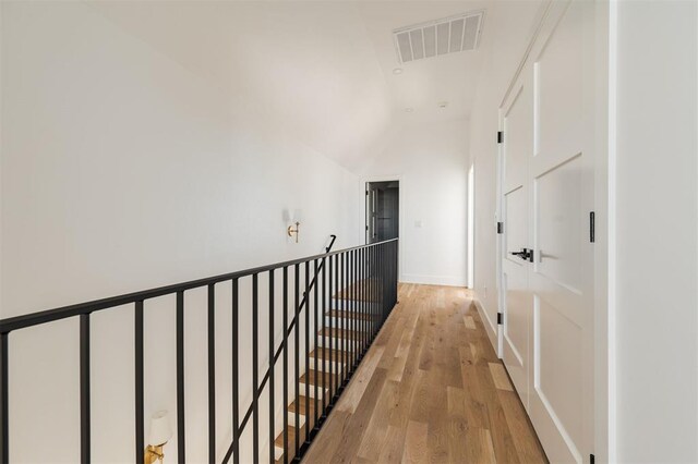 hallway with visible vents, lofted ceiling, baseboards, light wood-style floors, and an upstairs landing