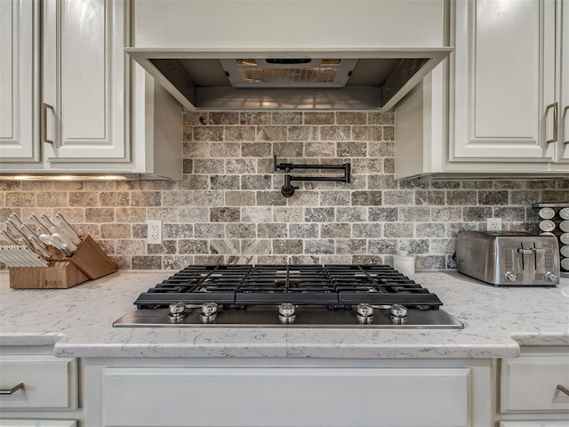 kitchen with light stone countertops, black gas cooktop, range hood, decorative backsplash, and white cabinets