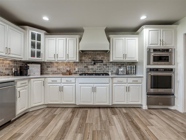 kitchen with light wood-type flooring, white cabinetry, premium range hood, and stainless steel appliances