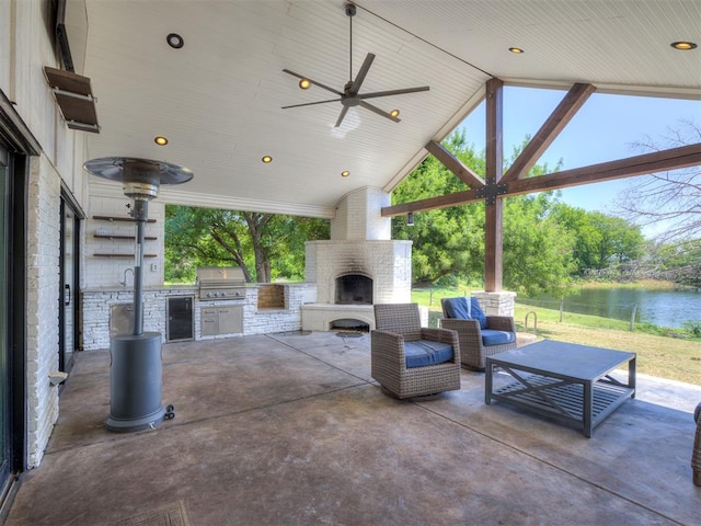 view of patio / terrace with ceiling fan, exterior kitchen, an outdoor living space with a fireplace, a water view, and grilling area