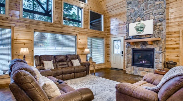 living room with wooden walls, high vaulted ceiling, a healthy amount of sunlight, and a stone fireplace