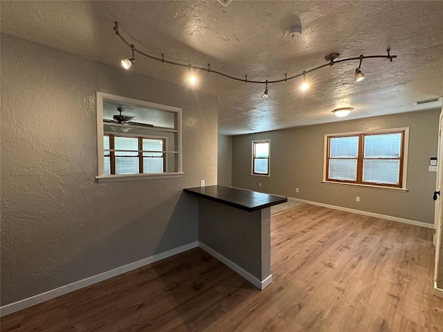 interior space with ceiling fan, kitchen peninsula, light hardwood / wood-style floors, a textured ceiling, and track lighting