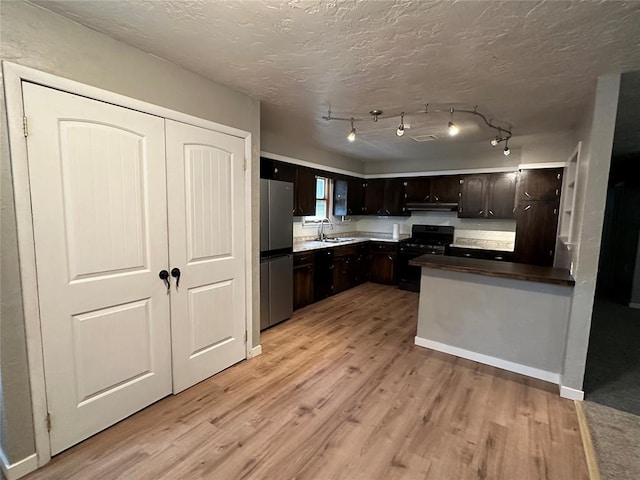 kitchen featuring black gas range, sink, stainless steel fridge, light wood-type flooring, and dark brown cabinets