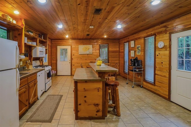 kitchen featuring a center island, white appliances, a breakfast bar area, wooden walls, and light tile patterned floors