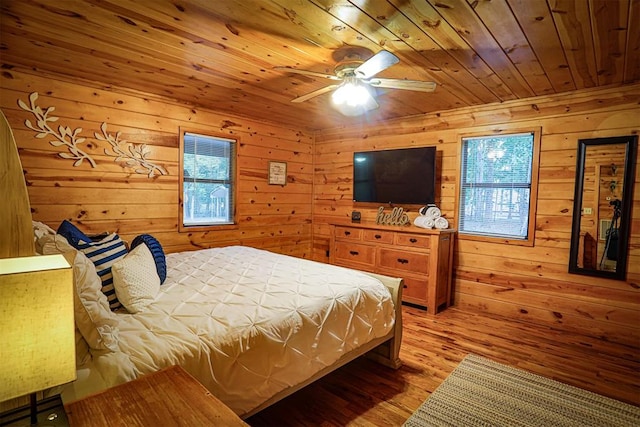 bedroom featuring ceiling fan, wood walls, light wood-type flooring, and multiple windows