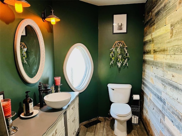 bathroom featuring toilet, vanity, hardwood / wood-style floors, and wood walls