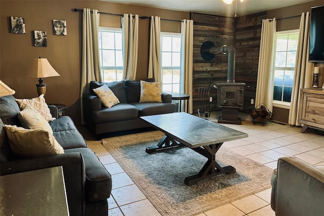 tiled living room with a wood stove, wooden walls, and a healthy amount of sunlight