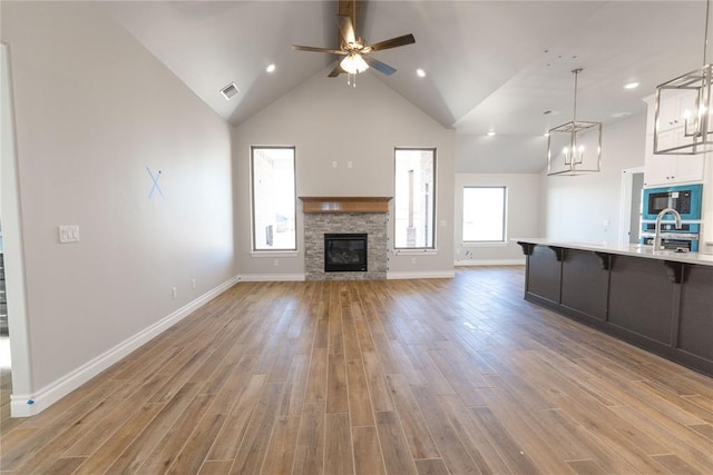 unfurnished living room with ceiling fan with notable chandelier, a fireplace, light hardwood / wood-style floors, and a wealth of natural light