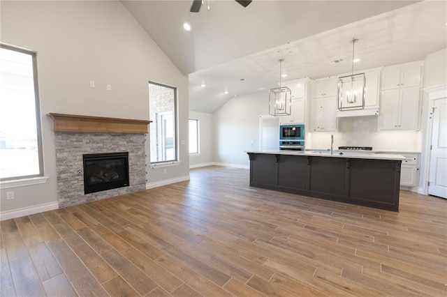 kitchen with hanging light fixtures, an island with sink, stainless steel oven, built in microwave, and white cabinetry