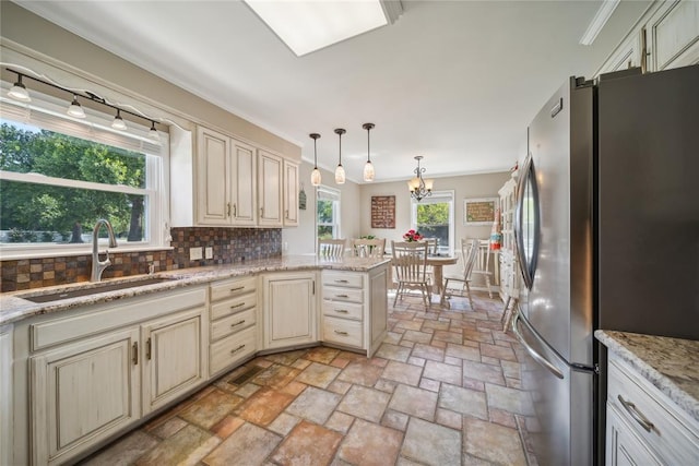 kitchen featuring backsplash, hanging light fixtures, sink, cream cabinetry, and stainless steel refrigerator