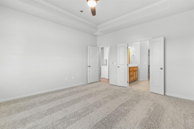 unfurnished bedroom with a tray ceiling, ensuite bath, ceiling fan, and light carpet