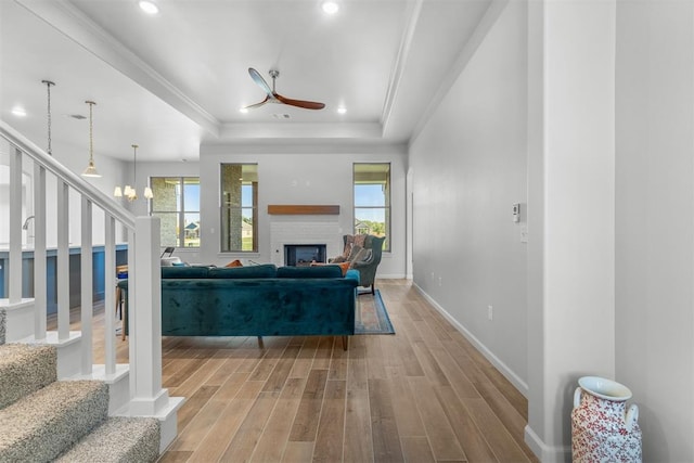 living room featuring ceiling fan with notable chandelier, a healthy amount of sunlight, a raised ceiling, and light hardwood / wood-style flooring