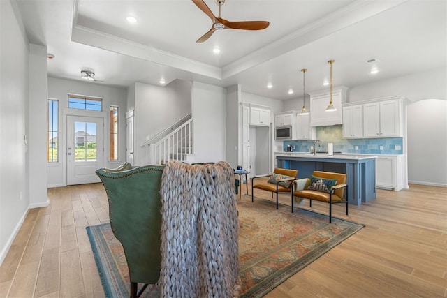 living room featuring light wood-type flooring, a raised ceiling, crown molding, and sink