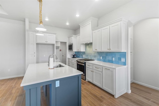 kitchen with sink, hanging light fixtures, stainless steel appliances, light hardwood / wood-style floors, and white cabinets